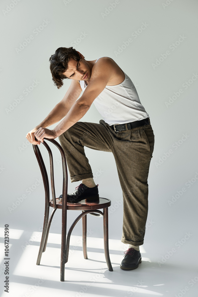 A young man in a tank top confidently poses on a chair, showcasing his tattoo against a soft grey background. A young man in a tank top confidently poses on a chair, showcasing his tattoo against a soft grey background.