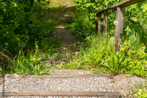 Old steep overgrown stairway with gravel leading down. An old wobbly railing provides a little safety. Beautiful sunshiny day. photo