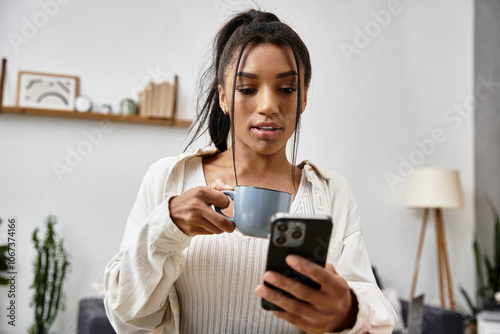 A student sips coffee and uses her smartphone while studying comfortably at home.