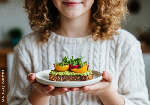 Smiling girl holding plate with avocado toast topped with tomatoes and microgreens