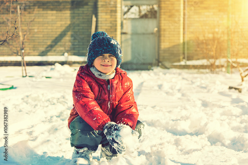 Excited Child playing with snow on white snow background. smiling boy catching snowflakes. Funny little boy in blue winter clothes walks during a snowfall. Outdoors winter activities for kids. toned