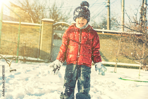 Excited Child playing with snow on white snow background. smiling boy catching snowflakes. Funny little boy in blue winter clothes walks during a snowfall. Outdoors winter activities for kids. toned