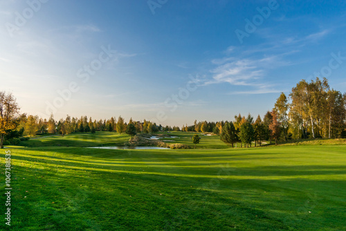 Magnificent view of the golf course with bright green grass and ponds on a clear autumn day.