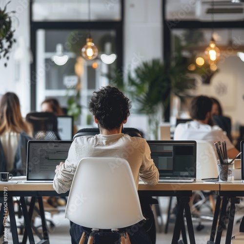 Rear view of computer programmers using laptop at office desk -