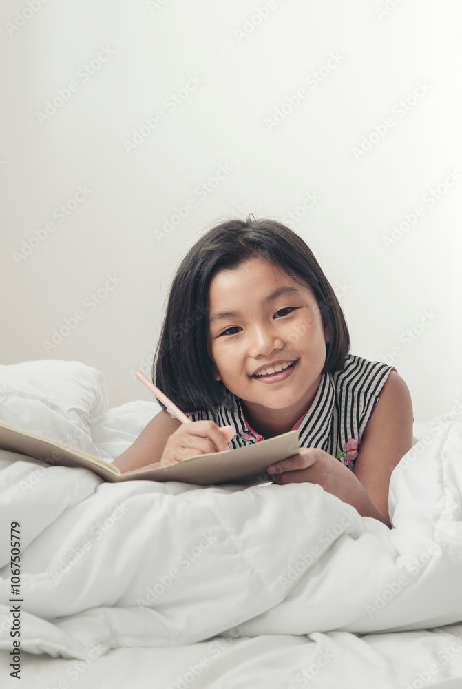 Asian Children Writing Letter on diary book. Kid learn and work, read book, girl lying in white bedroom at home. Cute Child doing and study homework. Little Child happy and smile. Education concept. Asian Children Writing Letter on diary book. Kid learn and work, read book, girl lying in white bedroom at home. Cute Child doing and study homework. Little Child happy and smile. Education concept.