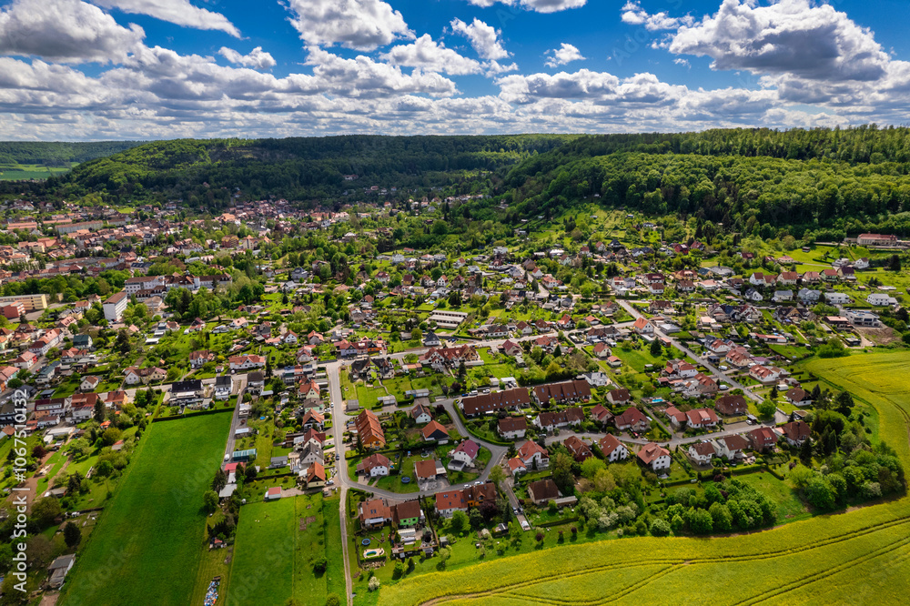 Top view of a field of yellow rapeseed flowers with a small town in the background. The sky is cloudy and the sun is shining through the clouds. Germany.