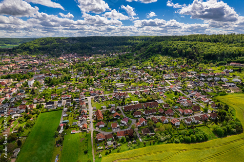Obraz na płótnie Top view of a field of yellow rapeseed flowers with a small town in the background. The sky is cloudy and the sun is shining through the clouds. Germany. w salonie