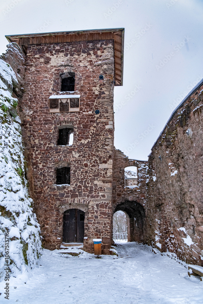 A castle with a snow covered roof and a steeple. The castle is surrounded by a snowy landscape. Ruin of Hohnstein Castle, Harz mountains, Germany.