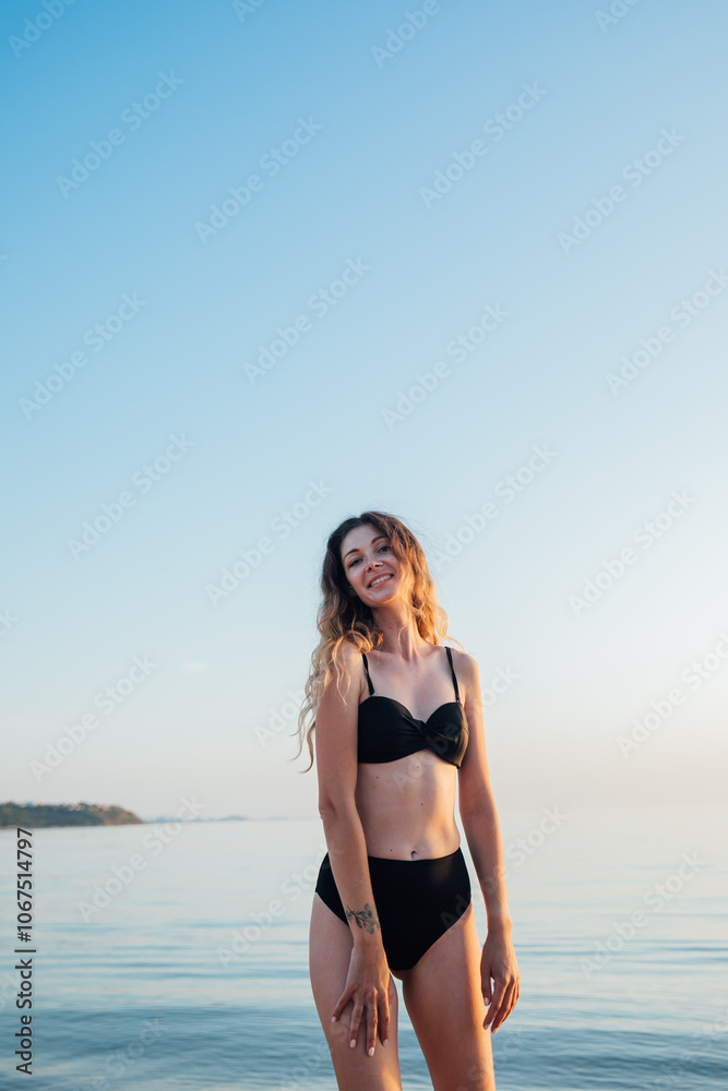 Portrait of a beautiful woman in a black swimsuit on the beach by the sea