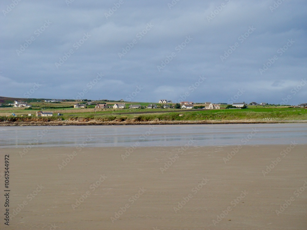 A scenic view showcasing a tranquil coastal village with charming houses, lush green fields, and a broad sandy beach under an overcast sky. Ideal for landscape, travel, and rural imagery. A scenic view showcasing a tranquil coastal village with charming houses, lush green fields, and a broad sandy beach under an overcast sky. Ideal for landscape, travel, and rural imagery.