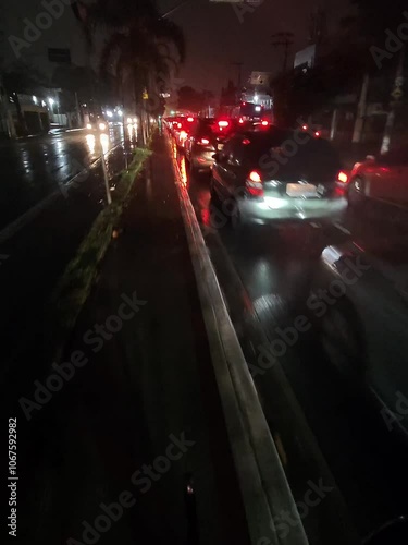 Cyclist riding through wet streets in São Paulo at night, reflecting city lights, on a rainy bike lane ride through busy urban traffic	