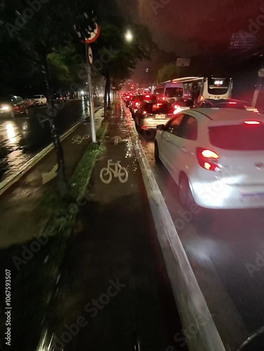 Urban cyclist braving rainy night in São Paulo, illuminated by city lights, pedaling through reflective wet streets	