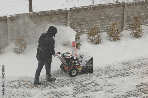 Worker clears snow from the sidewalk with a manual snowplow driven by a gasoline engine. Fighting the after-effects of a snowstorm. The power of the winter element
