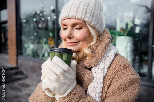 Photo of adorable cheerful lady dressed beige coat smelling tasty herbal tea aroma closed eyes outdoors residential complex