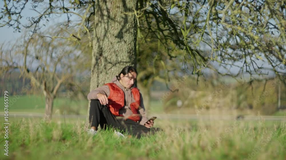 A person reading an electronic book outdoors under a tree, enjoying the sunlight and nature. Slow motion A person reading an electronic book outdoors under a tree, enjoying the sunlight and nature. Slow motion
