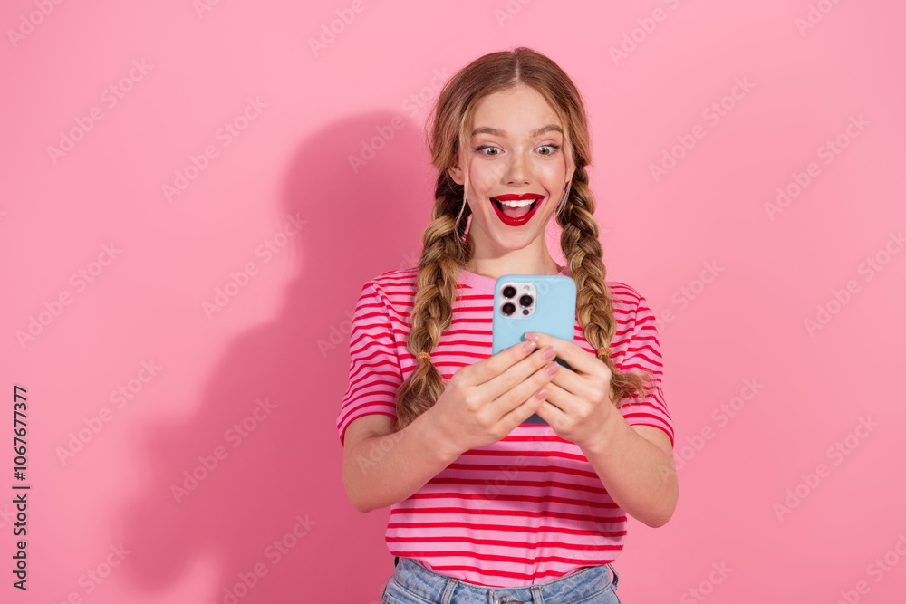 Young woman with braided hair excitedly holding phone against a vibrant pink background, showcasing youthful fashion and joy with charming red lipstick smile Young woman with braided hair excitedly holding phone against a vibrant pink background, showcasing youthful fashion and joy with charming red lipstick smile