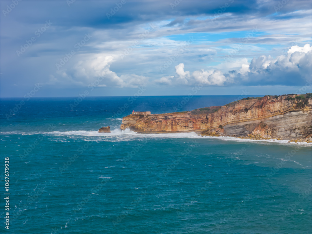 Nazare iconic cliff in Portugal where the biggest waves in the world are. Aerial drone view of cliff with lighthouse in Atlantic ocean Nazare iconic cliff in Portugal where the biggest waves in the world are. Aerial drone view of cliff with lighthouse in Atlantic ocean