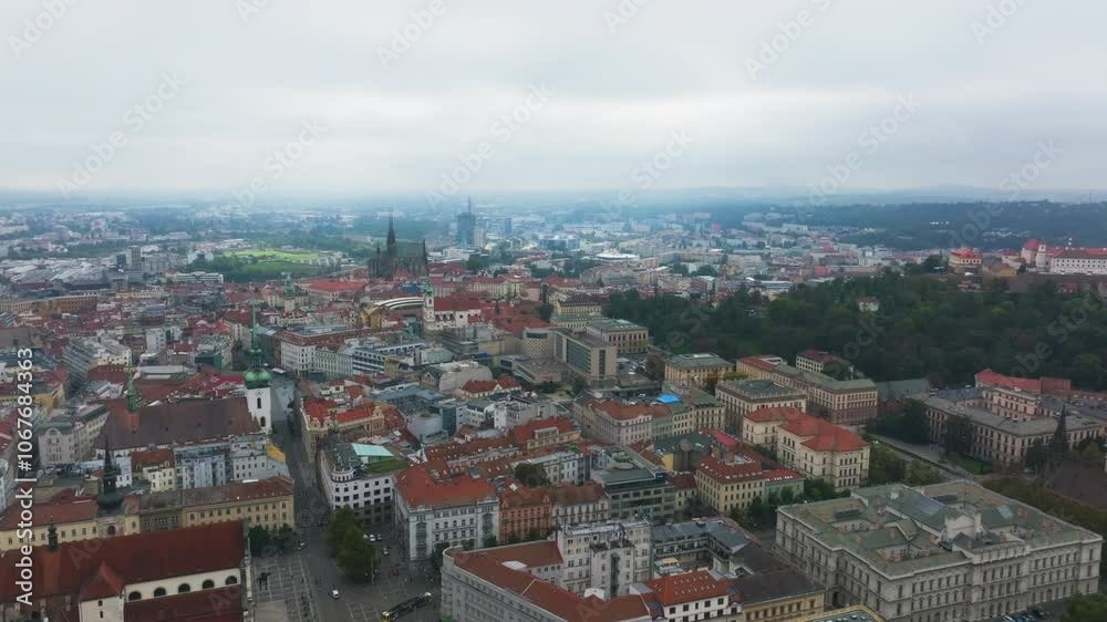 Aerial view panning across the Brno cityscape. Red rooftops and green spaces surround the towering Saint Thomas Church on a cloudy day Aerial view panning across the Brno cityscape. Red rooftops and green spaces surround the towering Saint Thomas Church on a cloudy day