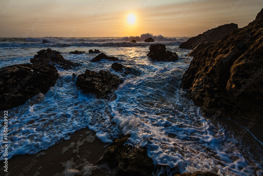 coastal sunset scene, waves rush in from the open sea, filling the space between the dark, rugged rocks coastal sunset scene, waves rush in from the open sea, filling the space between the dark, rugged rocks
