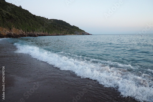 Waves gently lap at shore during stunning sunset over ocean. Sunlight reflects off waves as they roll onto shore, creating tranquil atmosphere at sunset by sea. Montenegro summer. Blue hour