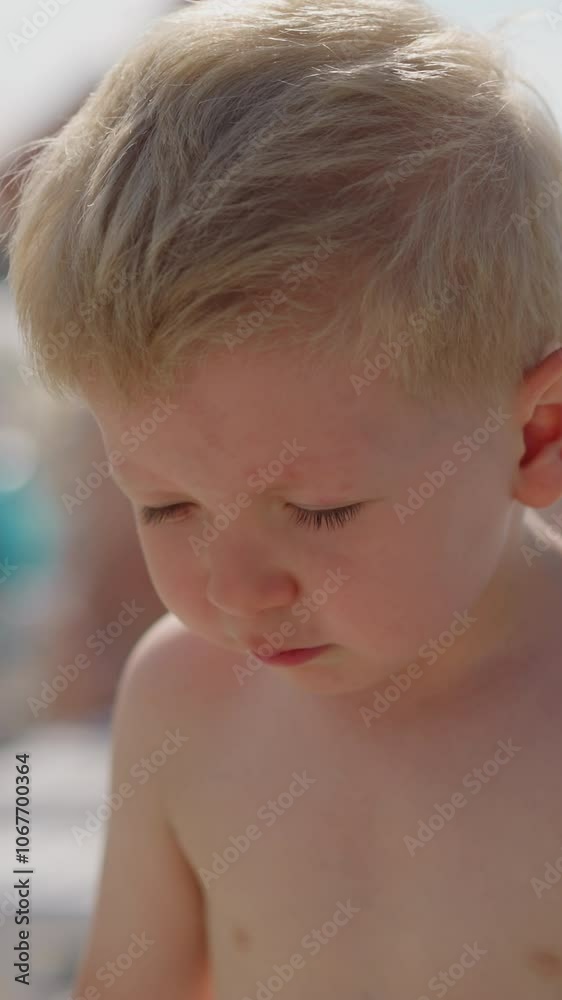Cute little toddler boy with bare chest sneezes and jumps spending time on beach at seaside resort on sunny summer day closeup slow motion Cute little toddler boy with bare chest sneezes and jumps spending time on beach at seaside resort on sunny summer day closeup slow motion