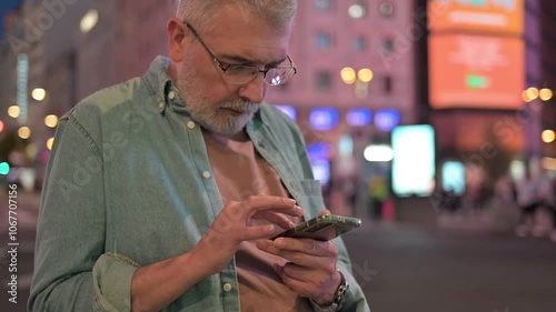 Elderly man with Parkinson’s deeply focused on his phone, capturing moments of connection.