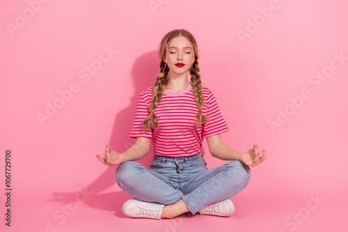 Charming young woman in striped t-shirt meditating on pink background with braided hair and red lipstick