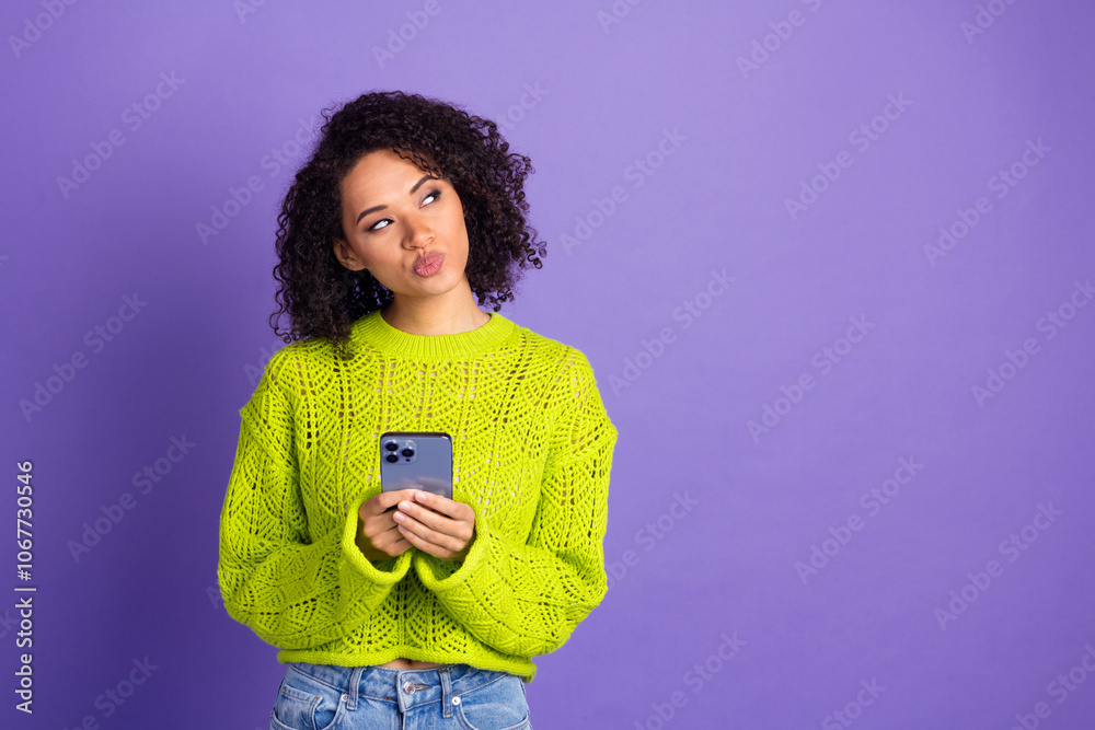 Photo of curly american young funky girl in green sweater using digital app smartphone looks thoughtful isolated on purple color background Photo of curly american young funky girl in green sweater using digital app smartphone looks thoughtful isolated on purple color background