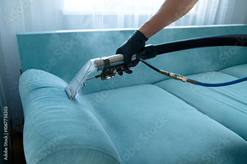 Cleaning concept. Man cleans sofa in the room. Virus prevention sanitizing inside. Process of deep furniture cleaning. Professionally chemical cleaning