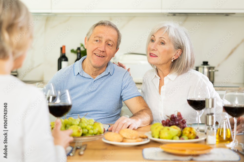 Happy pensioners gathered at the festive table - talking, discussing news and drinking red wine Happy pensioners gathered at the festive table - talking, discussing news and drinking red wine