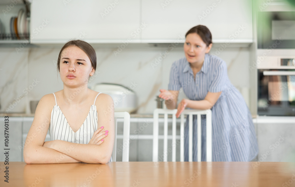 Upset daughter is sitting at table. Mom yells at her daughter in the background Upset daughter is sitting at table. Mom yells at her daughter in the background