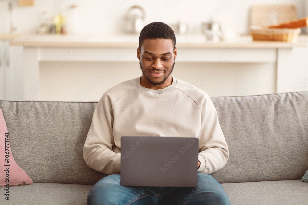 Portrait of bearded young black male freelancer working from home, sitting on couch, using laptop, copy space. Relaxed African American guy enjoying weekend, websurfing on notebook Portrait of bearded young black male freelancer working from home, sitting on couch, using laptop, copy space. Relaxed African American guy enjoying weekend, websurfing on notebook