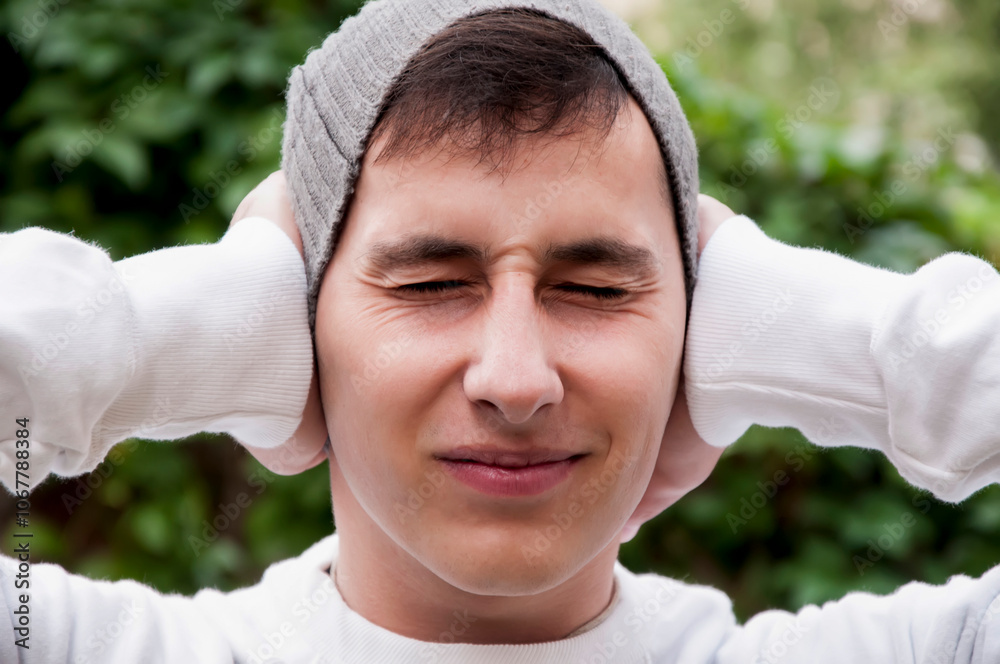 Portrait of young handsome man in park suffering from the pain in head