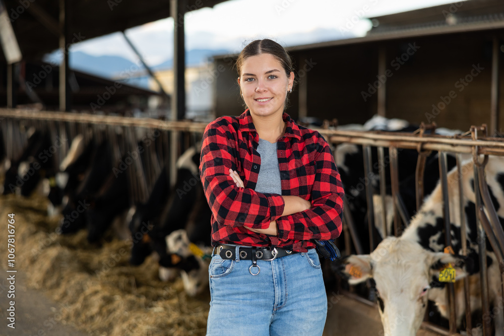 Φωτογραφία Positive young woman farmer standing in cowshed with arms crossed and smiling