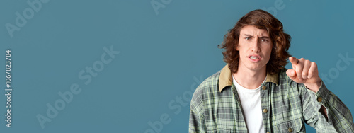 Frustrated teenager pointing finger at you in accusation on turquoise background