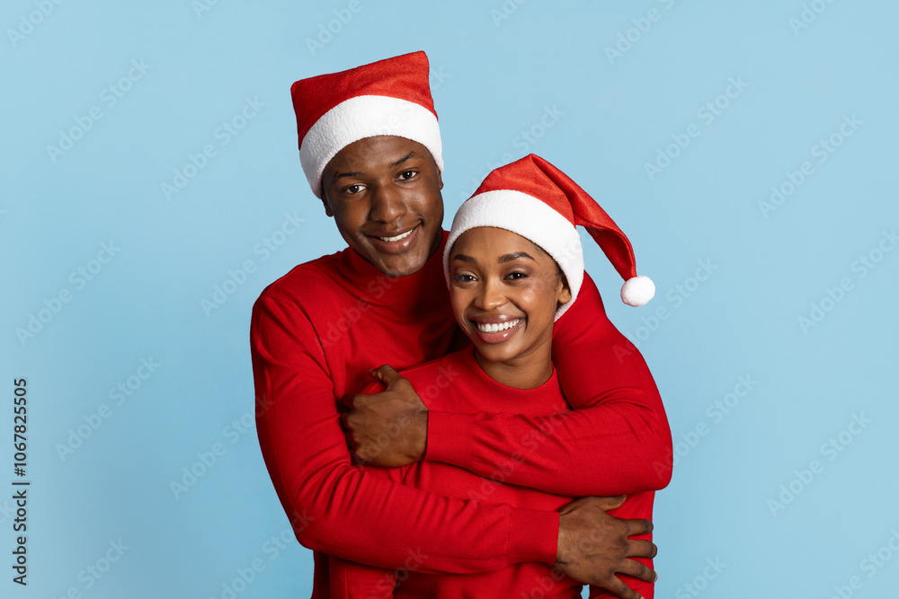 A joyful black couple embraces against a blue background, both wearing matching red sweaters and festive Santa hats. They radiate happiness and togetherness during the holiday season. A joyful black couple embraces against a blue background, both wearing matching red sweaters and festive Santa hats. They radiate happiness and togetherness during the holiday season.