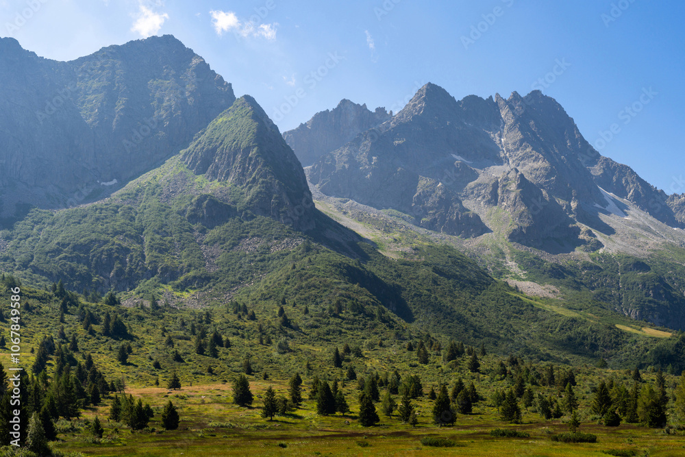 A breathtaking view of a towering mountain range with rugged peaks, verdant meadows, and dense pine forests under a clear blue sky, capturing the essence of natural beauty A breathtaking view of a towering mountain range with rugged peaks, verdant meadows, and dense pine forests under a clear blue sky, capturing the essence of natural beauty