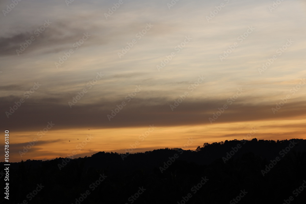 low hanging blue dark gray clouds hang low above rain forest covered hills as sunrise approaches low hanging blue dark gray clouds hang low above rain forest covered hills as sunrise approaches