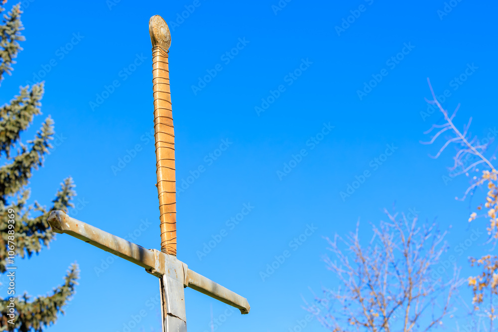 Fototapeta premium Metal sword sculpture with wrapped handle against a clear blue sky background