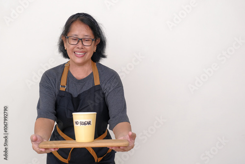 Asian housewife bringing a tray, with a yellow cup of hot drink with NO SUGAR writing on it photo