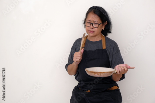 Asian housewife holding a frying pan and wooden spatula, wondering what to cook for dinner photo