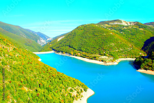 Magical scene from Lago di Fiastra (Lake Fiastra) with the rich azure blue colors of the waters extending through a smooth and unperturbed mirroring surface touching the shores amidst greenery photo