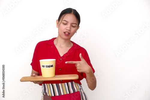 Asian female barista wearing red shirt bringing a tray, pointing her finger at yellow cup of hot drink with NO SUGAR writing on it photo