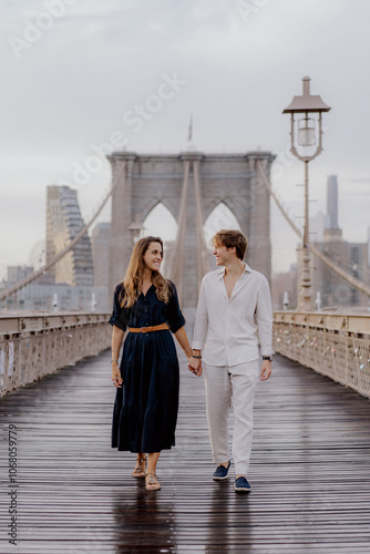 A couple strolls hand in hand on Brooklyn Bridge, surrounded by a stunning skyline and beautiful morning light