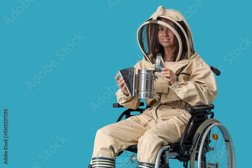 Female beekeeper in wheelchair with smoker on blue background photo