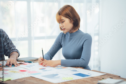 Focused on the Task: A young woman in a blue sweater intently analyzes data and diagrams, her expression focused and determined, reflecting the dedication and precision crucial to success.