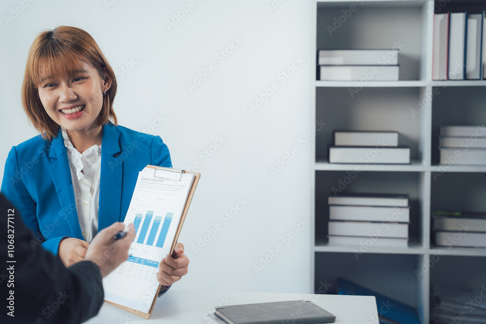 Businesswoman Discussing Charts: Two business professionals collaborate over a chart on a clipboard, showcasing their dedication to analyzing data and finding solutions in a modern office setting. Businesswoman Discussing Charts: Two business professionals collaborate over a chart on a clipboard, showcasing their dedication to analyzing data and finding solutions in a modern office setting.