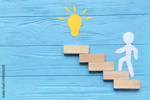Paper human figure with light bulb and blocks on blue wooden background. Coaching concept