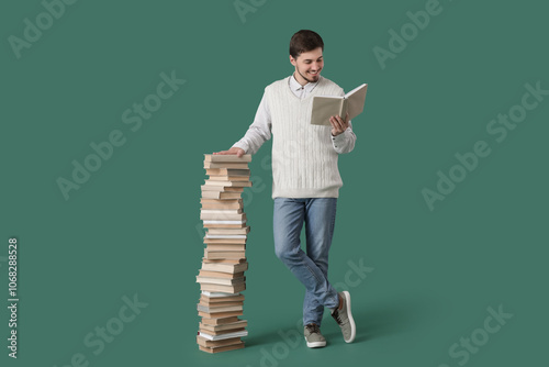 Young man with stack of books on green background