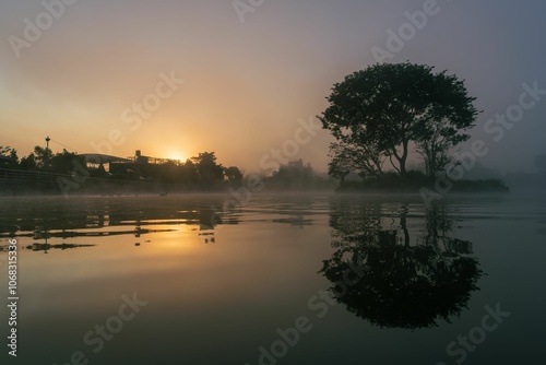 Serene sunrise over a misty lake with tree reflection.